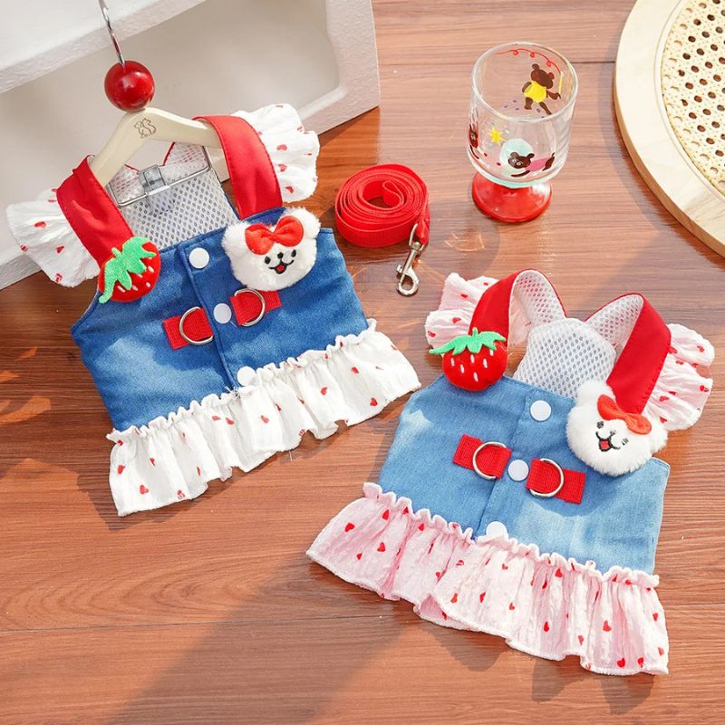 Two cat outfits with denim skirts, red bows, and strawberry details on a wooden surface.