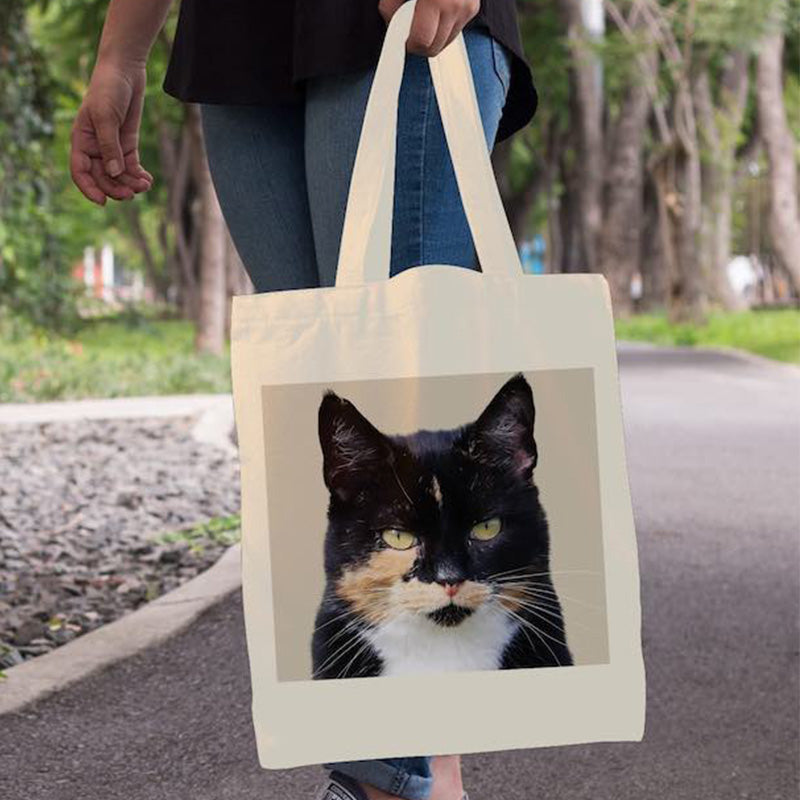 Tote bag with a cat's face printed on it held by a person outdoors.