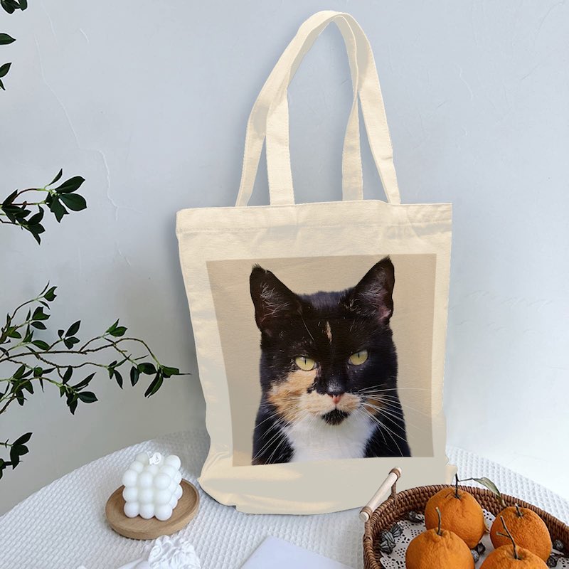 Tote bag with a cat's face printed on it, placed on a surface with decorative items.