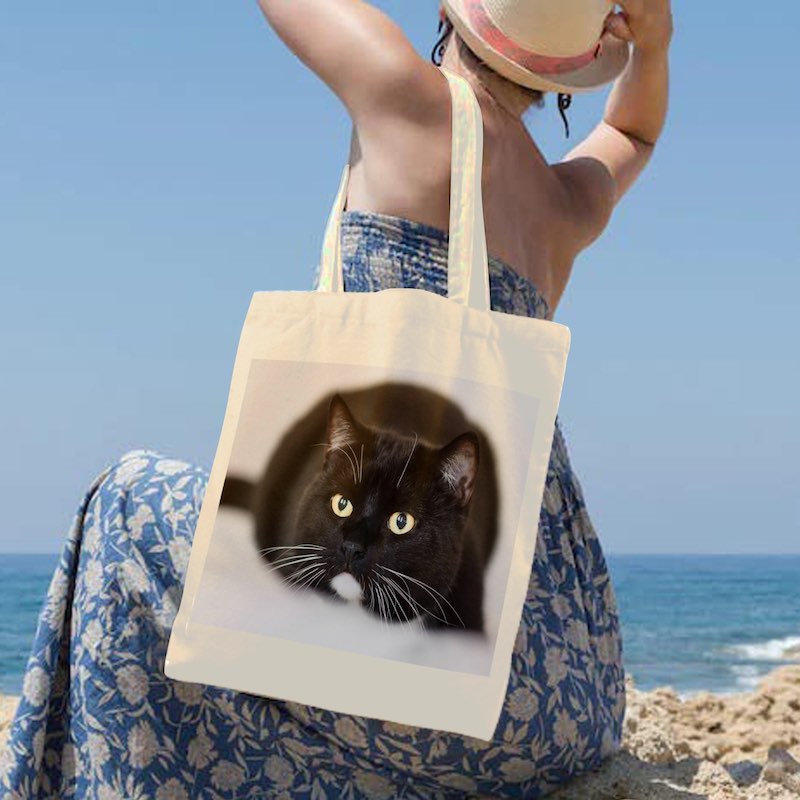 Person holding a tote bag with a cat design at the beach
