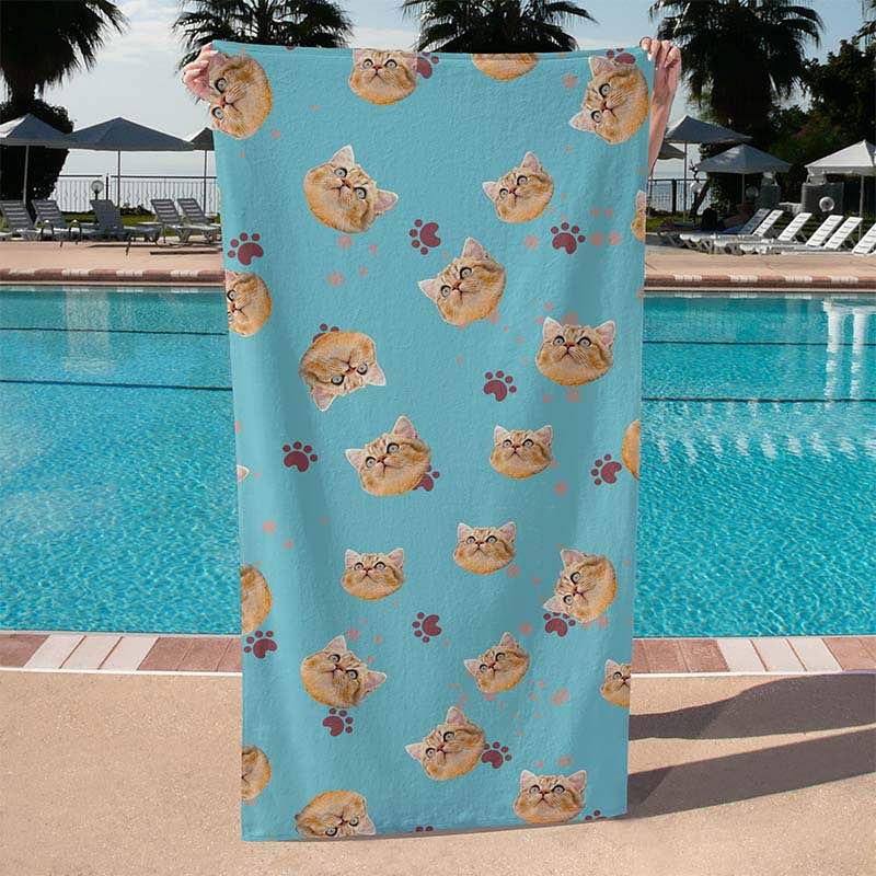 Light blue cat face print towel held up poolside with repeating pattern