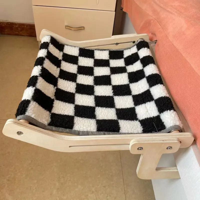 An empty wooden cat hammock with a black-and-white checkered pattern attached to a bed frame.