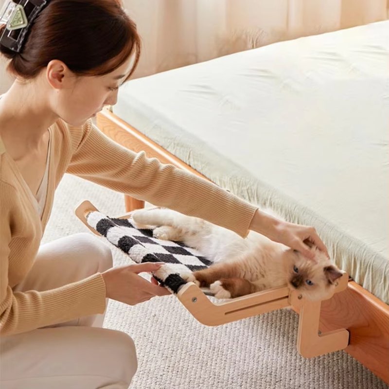 A woman petting a cat lying in a checkerboard hammock attached to a wooden bed.