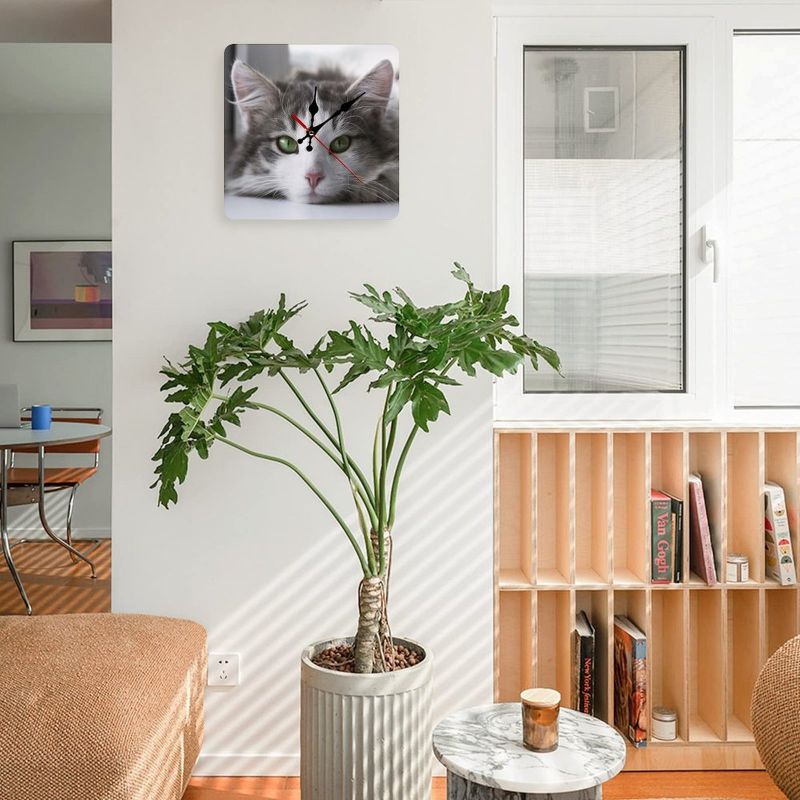 Cat-themed wall clock on a wall with a plant and books in the background